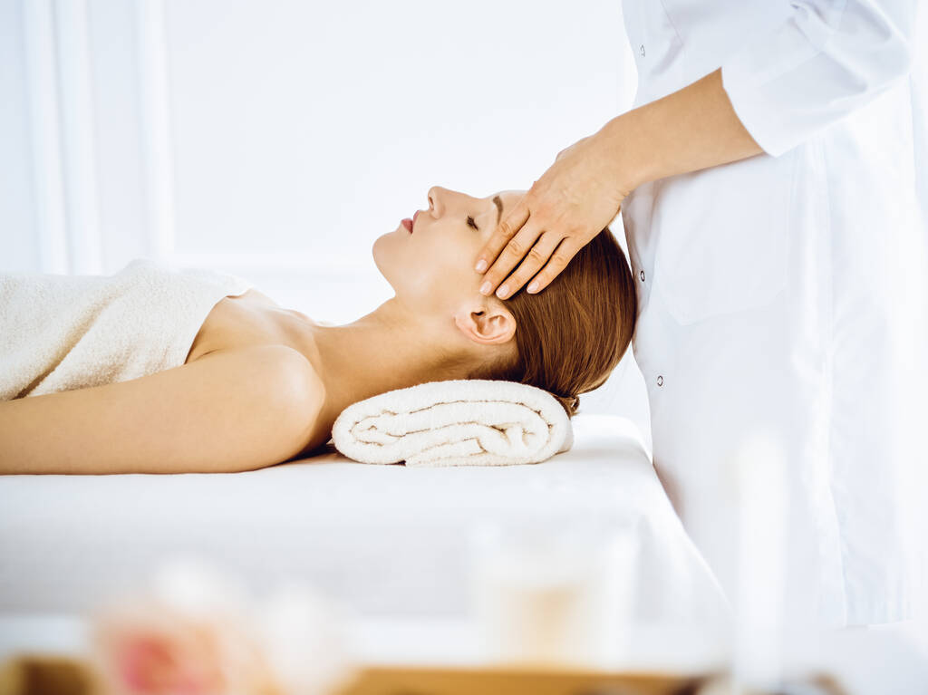 Hermosa mujer disfrutando de masaje facial con los ojos cerrados en el centro de spa - Foto, imagen