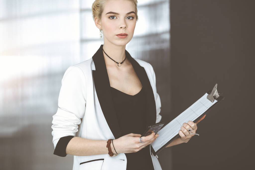 Fiatal szőke üzletasszony vagy fehér öltönyös diáklány áll a modern irodában. Életmód és sokszínű emberek koncepciója - Fotó, kép