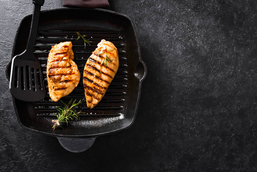 Grillezett csirkemell filé grill serpenyőben rozmaringgal, felülnézet, másolás helyet. Grillezett hús steak rusztikus fekete háttér. - Fotó, kép