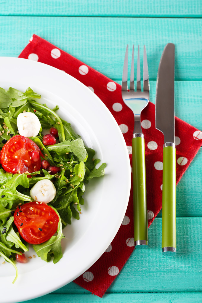 Salada verde feita com arugula, tomates, bolas de mussarela de queijo e gergelim na placa, na cor de fundo de madeira
 - Foto, Imagem