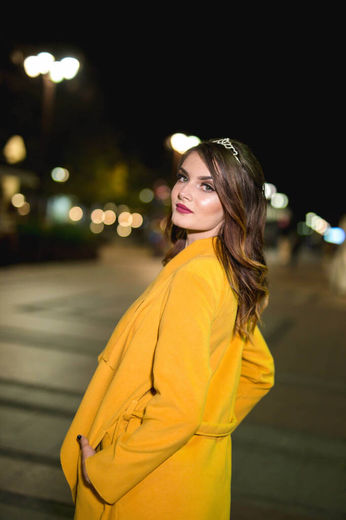 Krásná a elegantní běloška v černých šatech a žlutém kabátě pózující v noci na ulici - Fotografie, Obrázek
