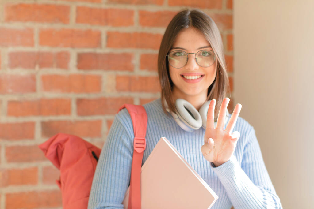 estudante bonita sorrindo e olhando amigável, mostrando o número três ou terceiro com a mão para a frente, contando para baixo - Foto, Imagem