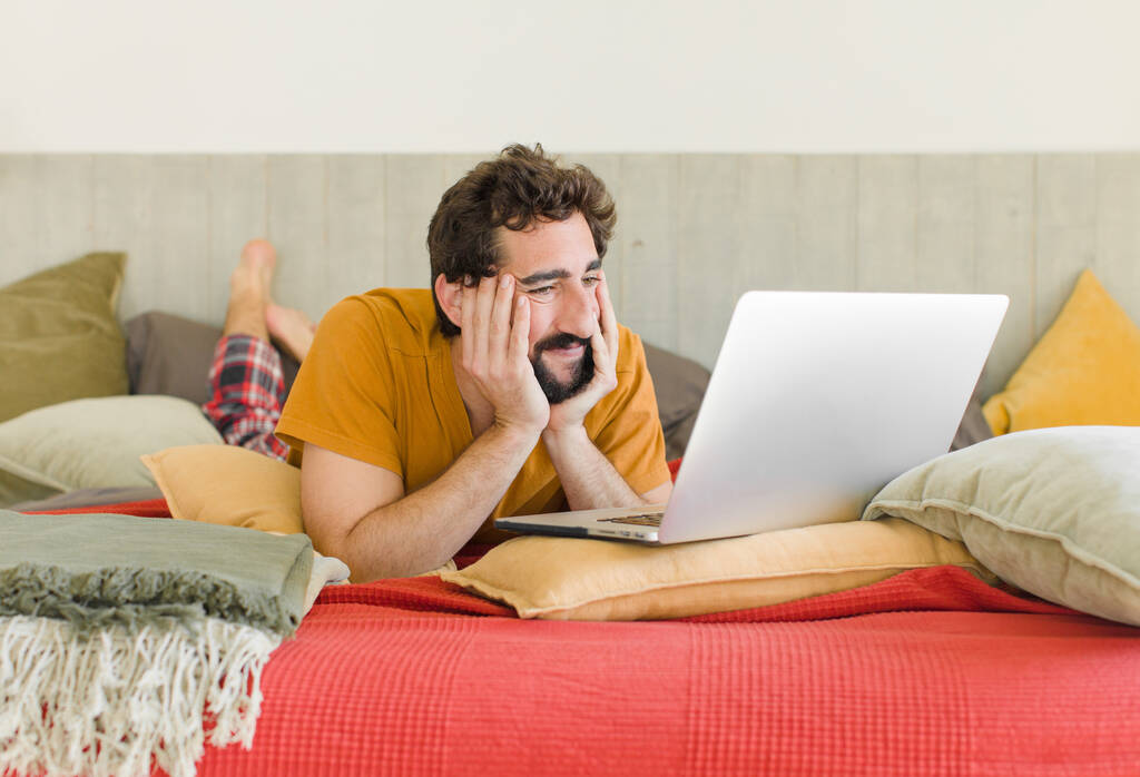 joven barbudo en una cama con un ordenador portátil - Foto, imagen