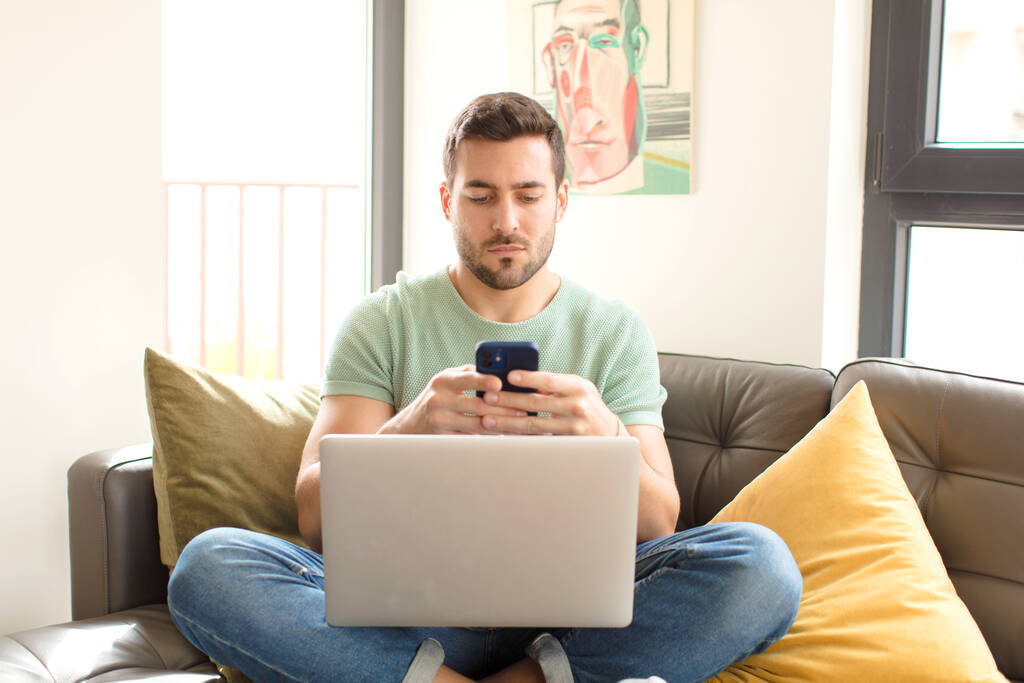 νεαρός όμορφος άντρας χρησιμοποιεί το smartphone του στο σπίτι - Φωτογραφία, εικόνα