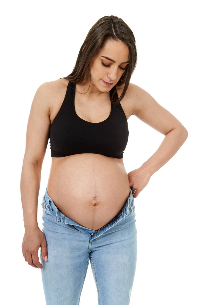 Pregnant woman trying to fit in her too tight jeans, isolated on white background - Photo, Image