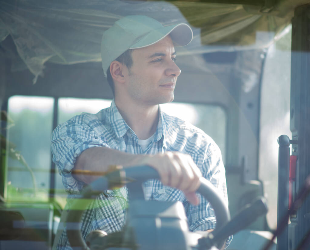 Sonriente joven agricultor conduciendo un tractor - Foto, Imagen