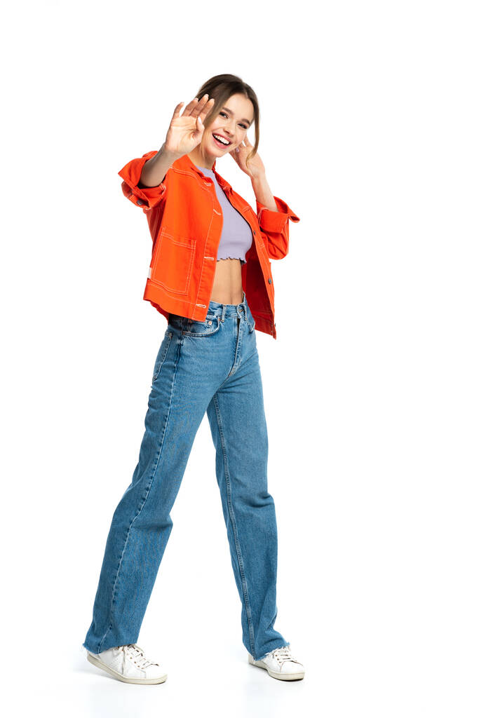 volledige lengte van gelukkige jonge vrouw in gewas top en oranje shirt gebaren geïsoleerd op wit  - Foto, afbeelding