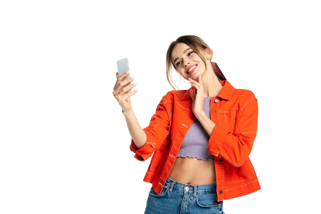 Kırpılmış bluzlu ve turuncu tişörtlü genç bir kadın beyaz telefondan selfie çekiyor. - Fotoğraf, Görsel
