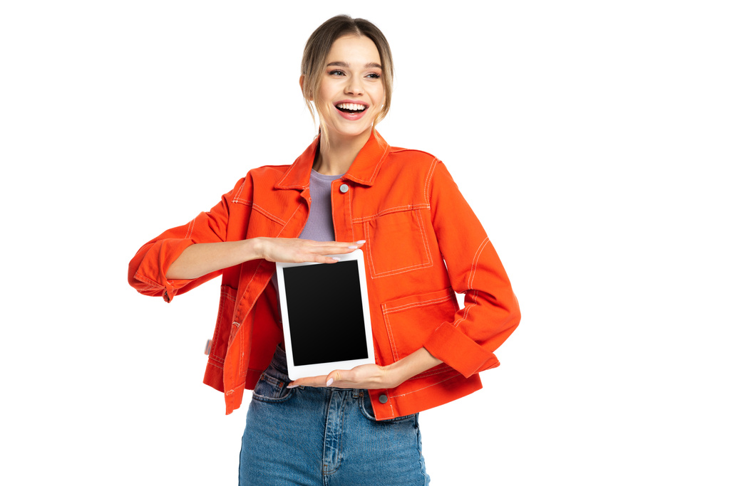 счастливая молодая женщина в оранжевой рубашке и джинсах проведение цифровой планшет с чистым экраном изолированы на белом - Фото, изображение