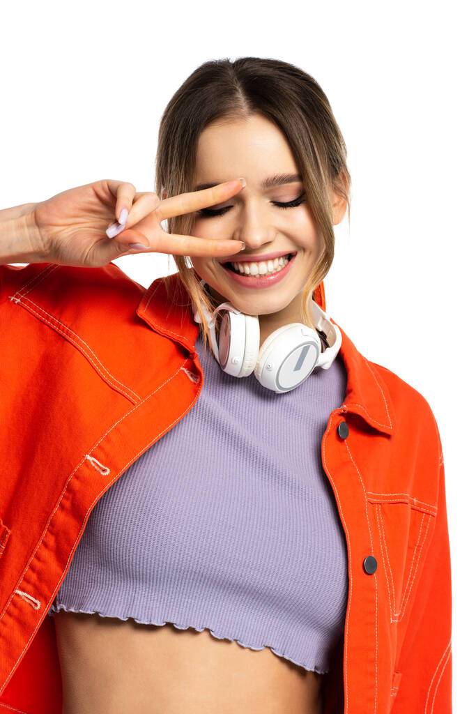オレンジ色のシャツを着た喜びの女性と白に隔離された平和サインを示す無線ヘッドフォン - 写真・画像