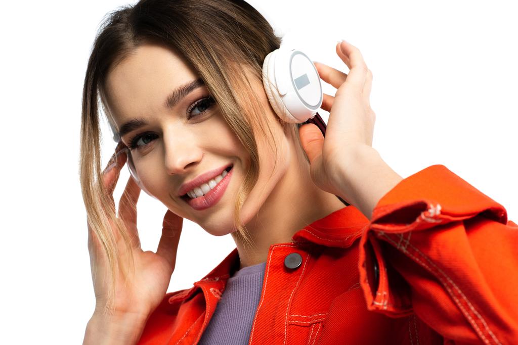 potěšená žena v oranžové košili poslech hudby v bezdrátových sluchátkách izolovaných na bílém - Fotografie, Obrázek