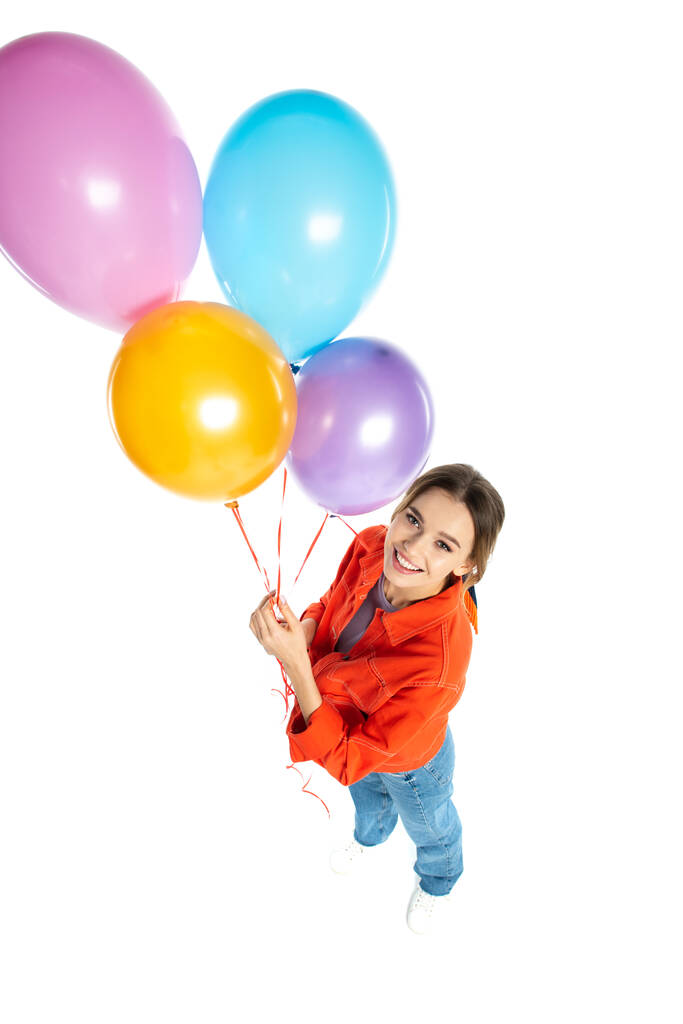 visão de alto ângulo da jovem mulher feliz na camisa laranja segurando balões coloridos isolados no branco - Foto, Imagem