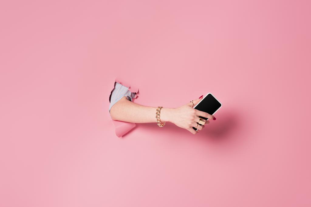 Обрезанный вид женщины с мобильным телефоном рядом розовый фон с отверстием  - Фото, изображение