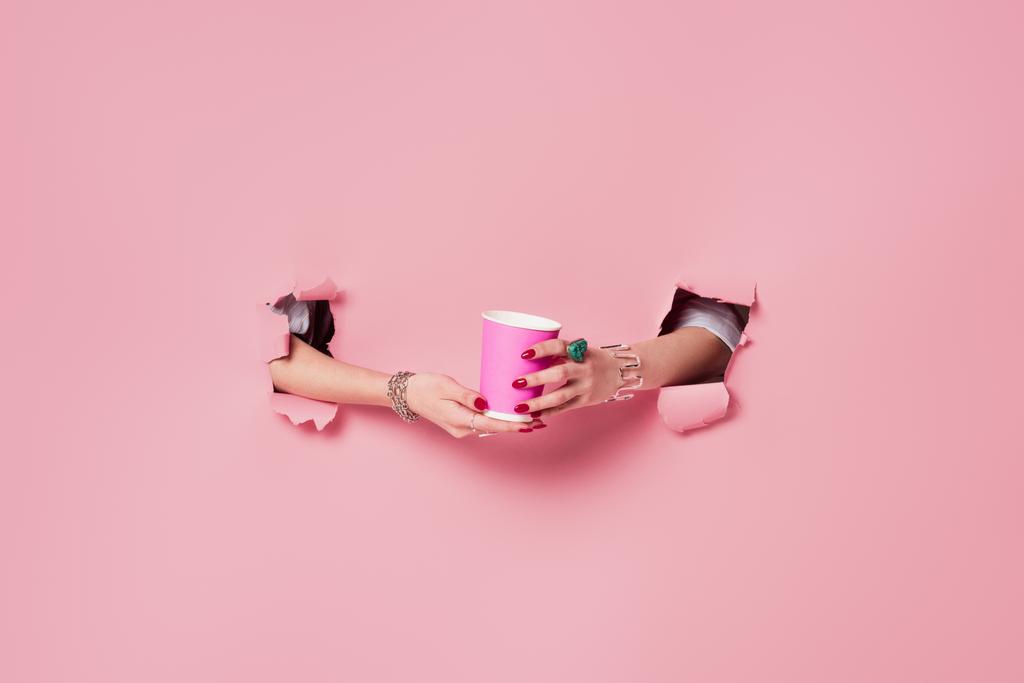 Cropped view of woman holding coffee to go in holes of pink background  - Photo, Image