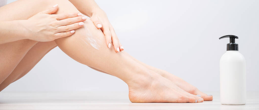 La mujer aplica crema hidratante a sus piernas sobre un fondo blanco. La chica cuida la piel y usa la crema. - Foto, imagen