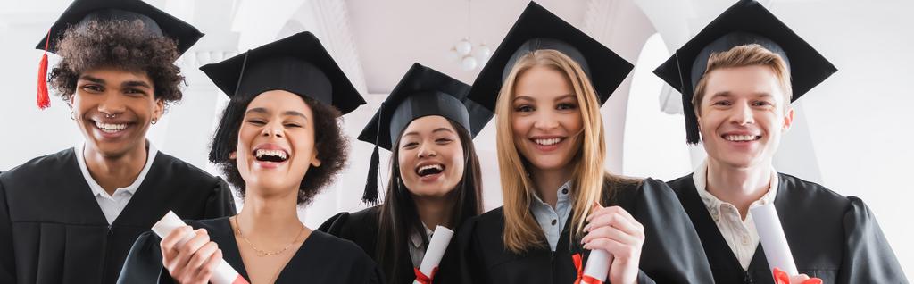 Багатоетнічні студенти в шапках тримають дипломи і посміхаються на камеру, банер
  - Фото, зображення