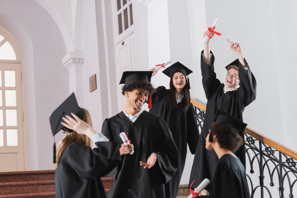 Opgewonden afgestudeerde wijzend naar diploma in de buurt van interraciale vrienden  - Foto, afbeelding