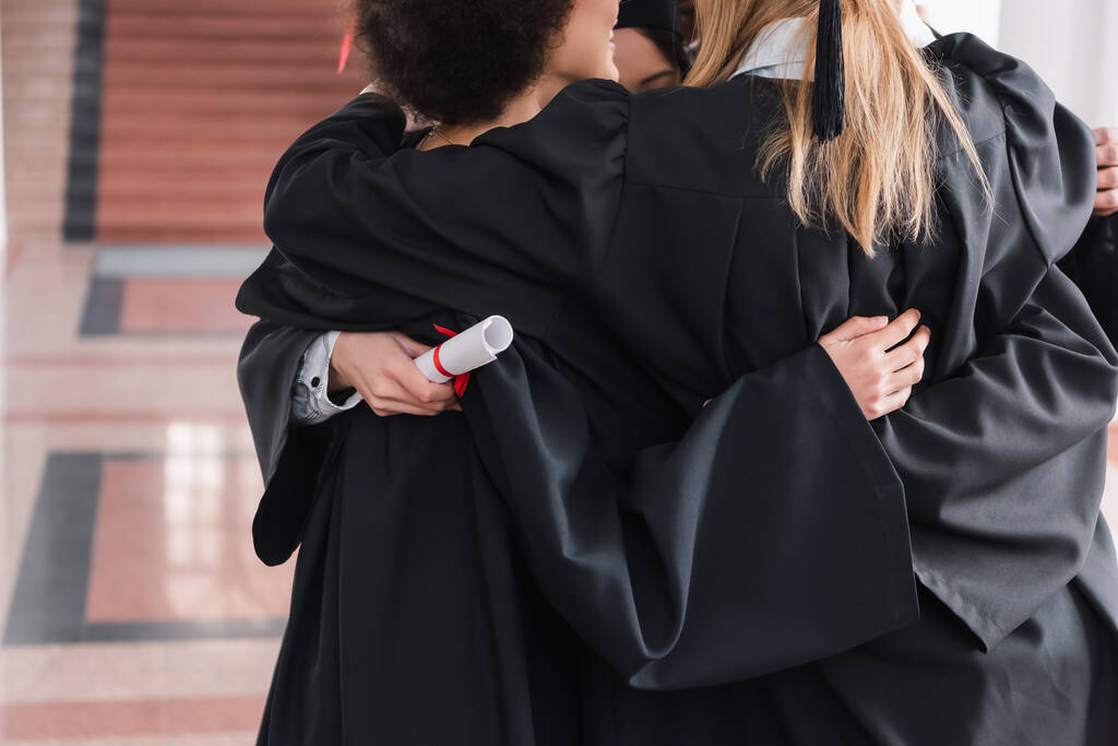 Vista ritagliata di laureati interrazziale abbracciare in università  - Foto, immagini