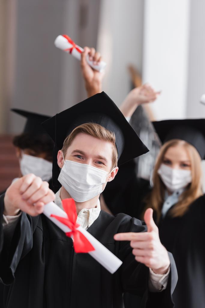 Diplômé en masque médical pointant vers un diplôme flou  - Photo, image