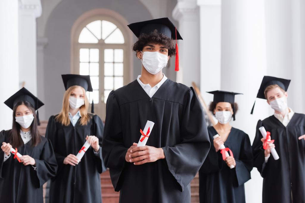 Afroamerikanische Absolventin in medizinischer Maske und akademischer Kleidung mit Diplom  - Foto, Bild