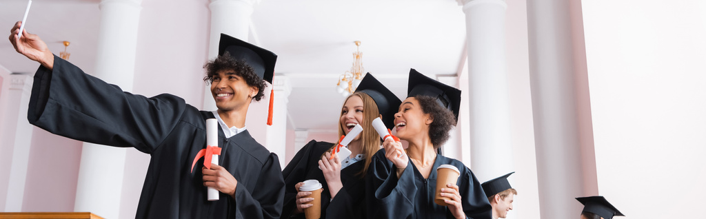 Smiling multiethnic graduates with paper cups taking selfie, banner  - Photo, Image