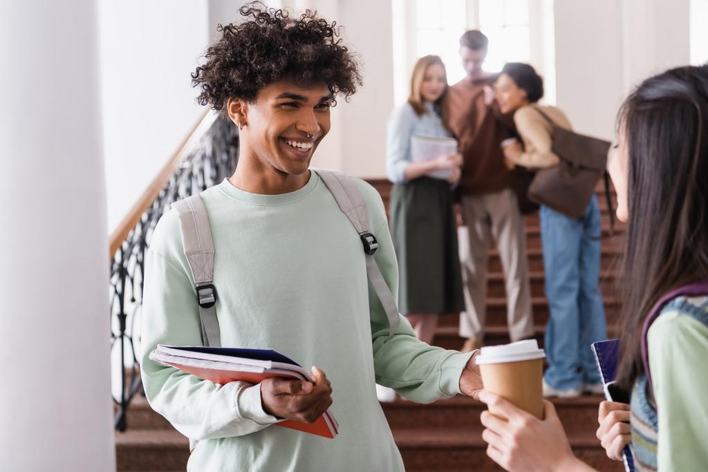 Usmívající se africký americký student s notebooky mluvit s asijské přítel s kávou jít  - Fotografie, Obrázek