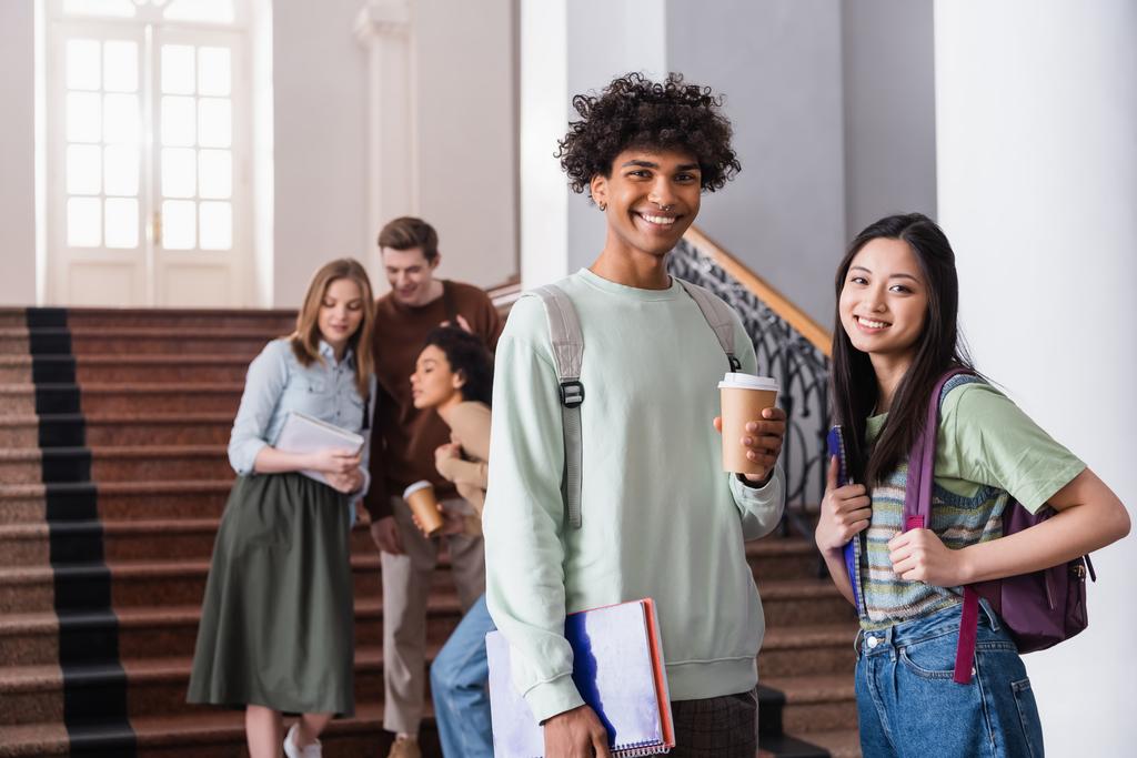 Мультиэтнические студенты с рюкзаками и кофе будут улыбаться в университете  - Фото, изображение