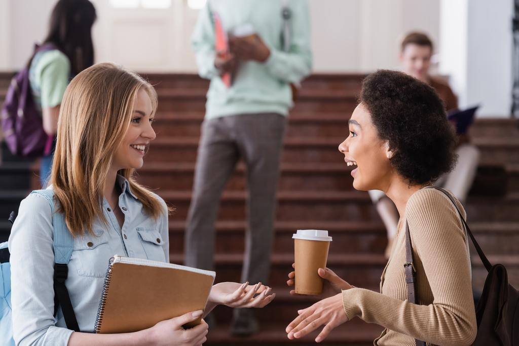 Positieve interraciale studenten met notebook en koffie praten  - Foto, afbeelding