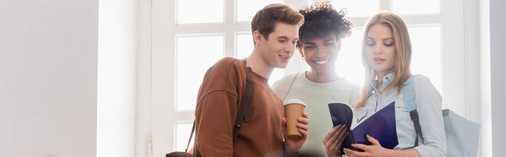 Interracial students with coffee to go and notebook standing near window, banner  - Photo, Image