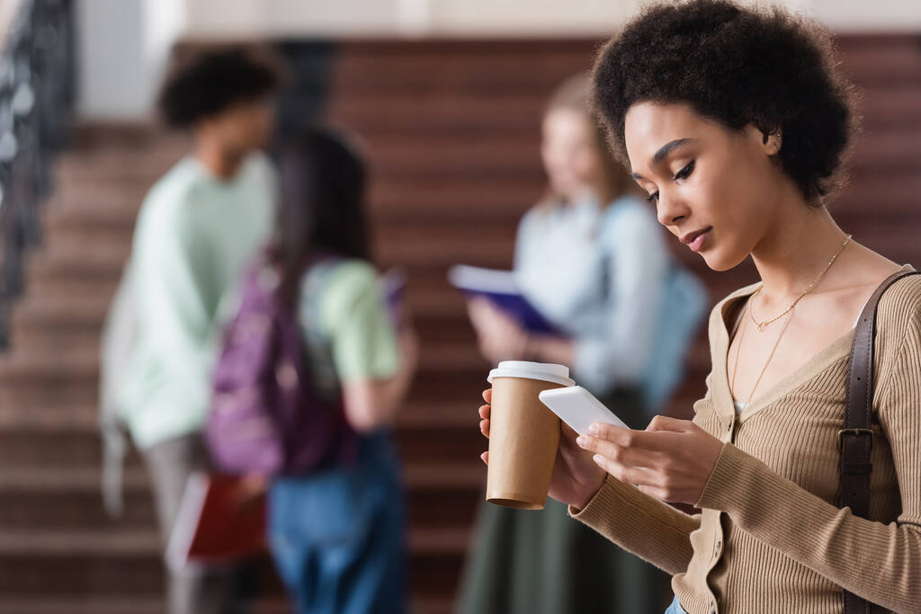 Afroamerikanische Studentin mit Coffee to go per Smartphone  - Foto, Bild