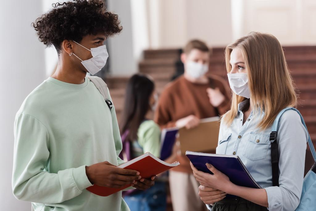 Wieloetniczni studenci w maskach medycznych trzymający notatniki na uniwersytecie  - Zdjęcie, obraz