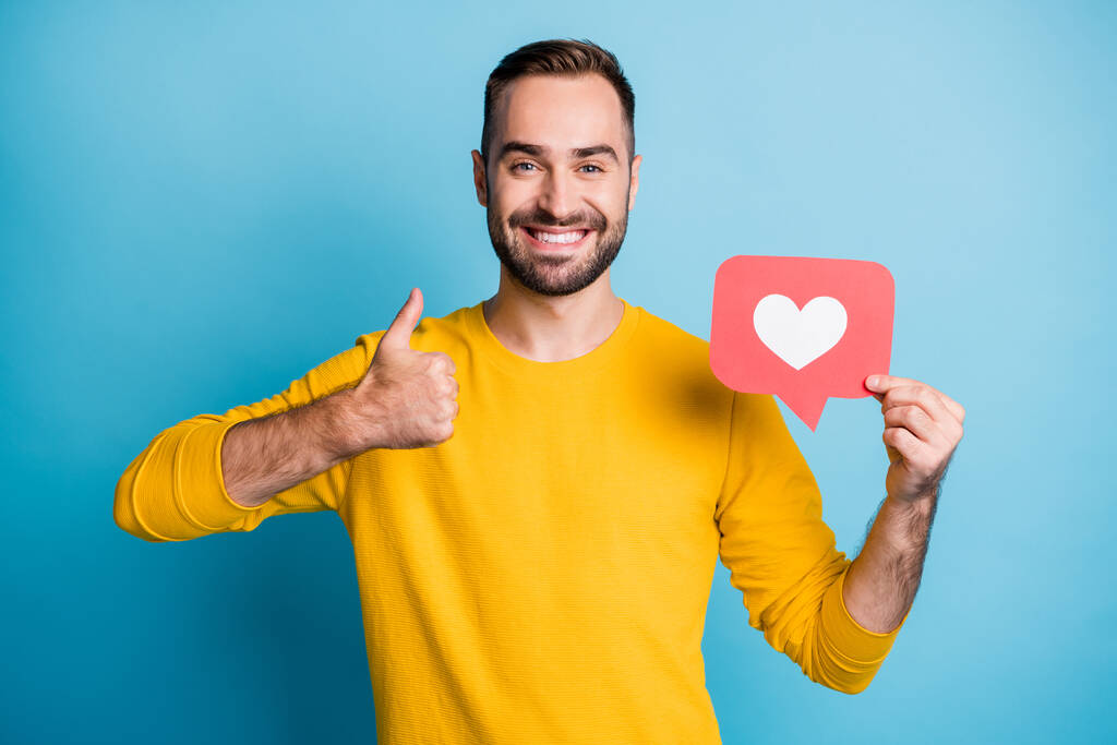 Retrato fotográfico del bloguero manteniendo el icono del corazón comentarios en las redes sociales mostrando como un signo aislado en un fondo de color azul vivo - Foto, imagen