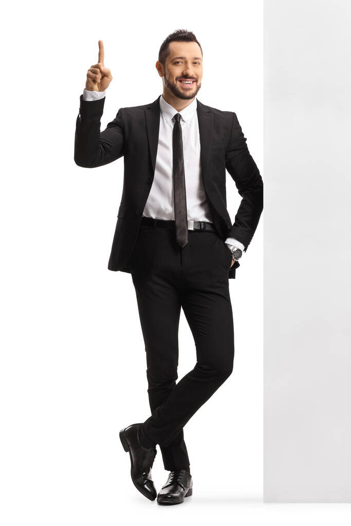 Homem profissional em um terno e gravata inclinada em uma parede e apontando para cima isolado no fundo branco - Foto, Imagem