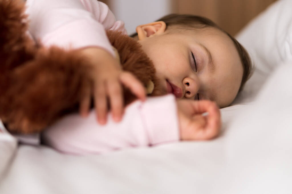 Authentiek portret schattig Kaukasisch klein baby mollig meisje of jongen in roze slaap met teddybeer op wit bed. kind rust uit rond lunchtijd. verzorging, Slaapkind, Jeugd, Ouderschap, levensloop - Foto, afbeelding
