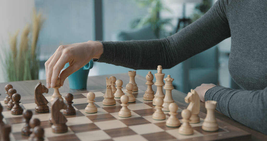 Frau spielt Schach zu Hause, sie bewegt einen Bauern auf dem Schachbrett - Foto, Bild