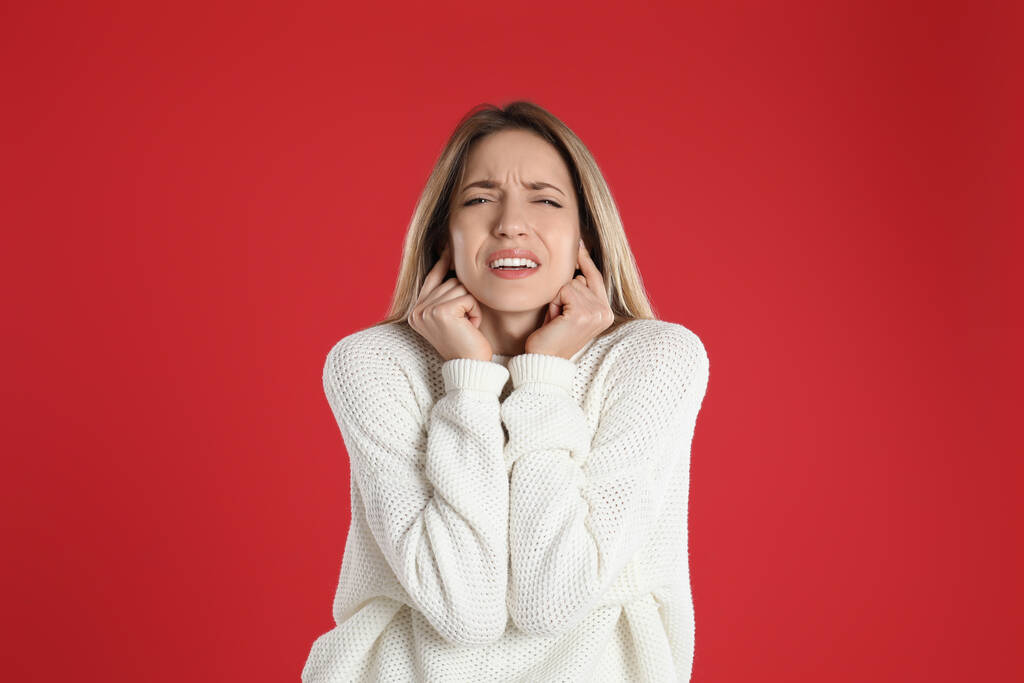 Емоційна молода жінка прикриває вуха пальцями на червоному тлі
 - Фото, зображення