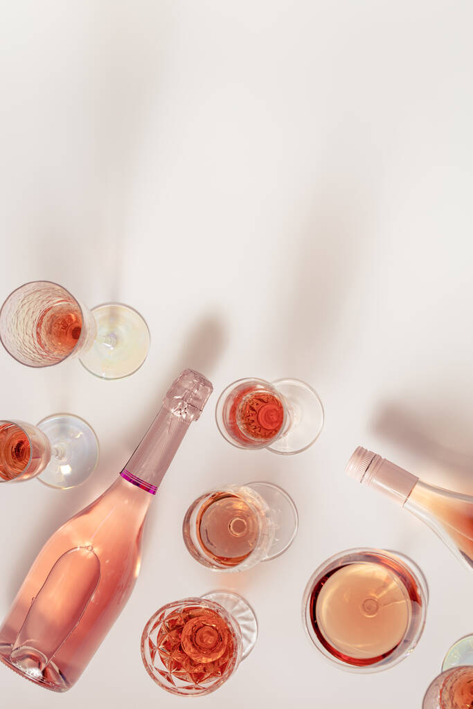 Πολλά ποτήρια ροζέ κρασί και μπουκάλι αφρώδες ροζ κρασί πάνω όψη. Ελαφρύ ποτό για πάρτι. Επίπεδη θέσει σε ελαφρύ τραπέζι την ημέρα του καλοκαιριού. - Φωτογραφία, εικόνα