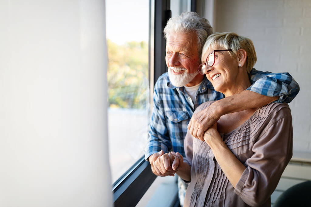 Счастливая улыбающаяся пожилая пара обнимается вместе и наслаждается уходом на пенсию дома - Фото, изображение