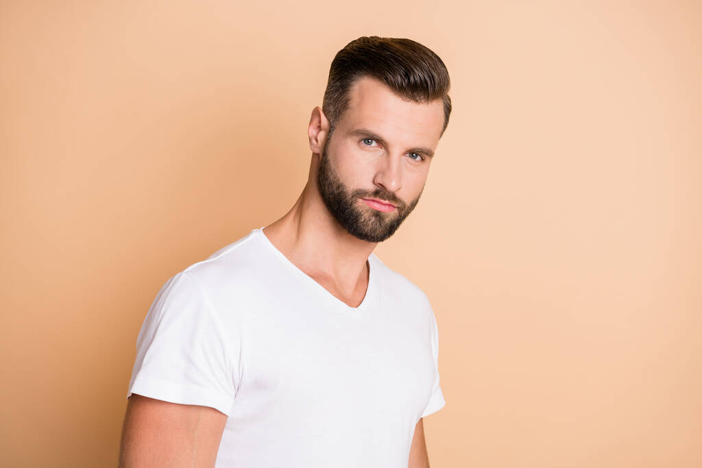 Fotografie mladého pohledného strniště muž vážné sebevědomí nosit bílé tričko izolované přes béžové barvy pozadí - Fotografie, Obrázek