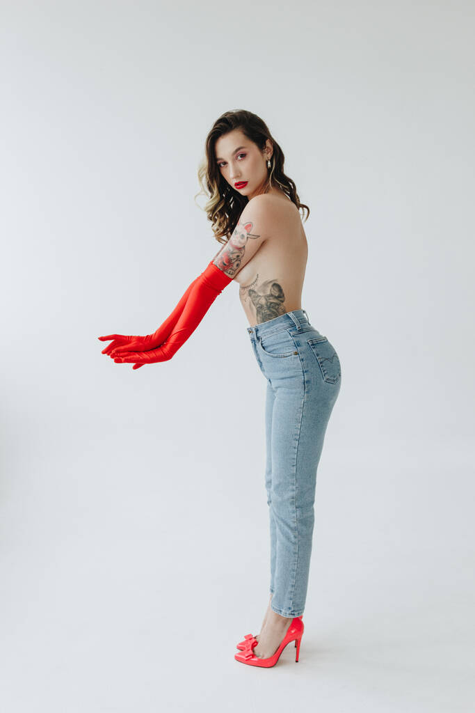 Donna sexy con tatuaggi che indossano jeans e guanti rossi su sfondo bianco - Foto, immagini