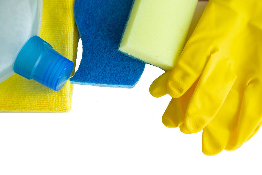 The cleaning agent lies on the yellow terry cloth on the side, sponge rags and gloves lie on top on a white background - Photo, Image