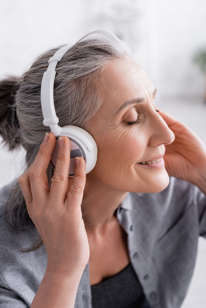 Mutlu orta yaşlı kadın kablosuz kulaklıkla müzik dinliyor.  - Fotoğraf, Görsel