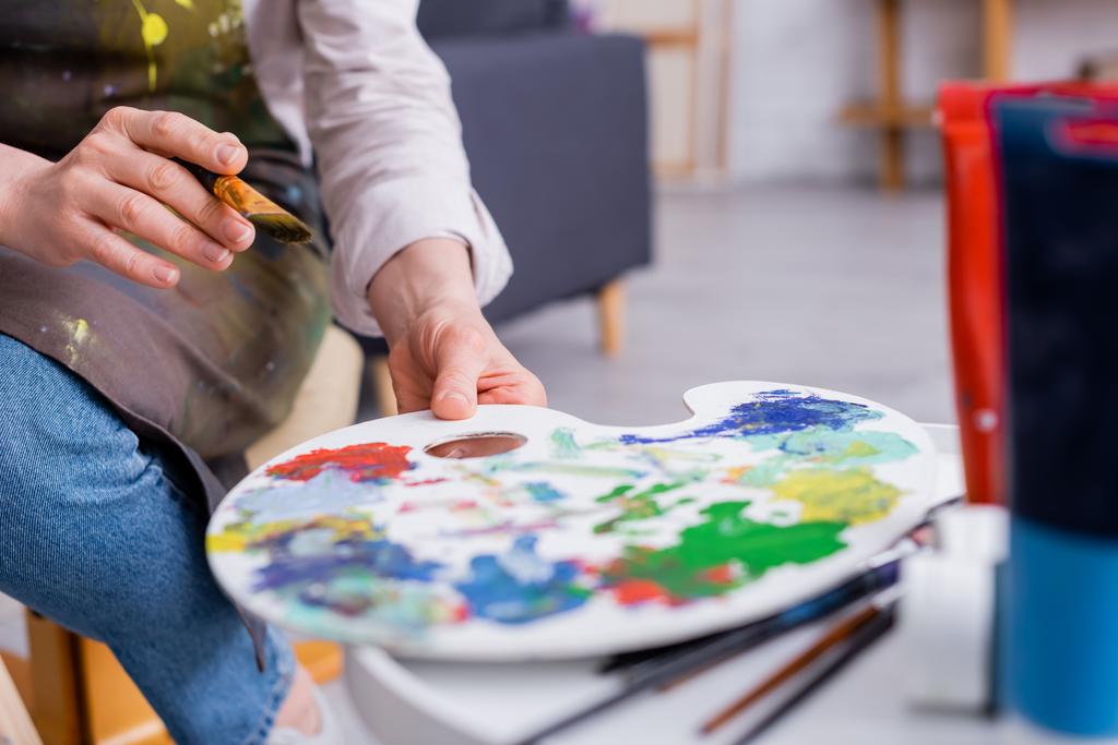 Ausgeschnittene Ansicht eines Künstlers mittleren Alters mit Pinsel und Palette mit bunten Farben  - Foto, Bild
