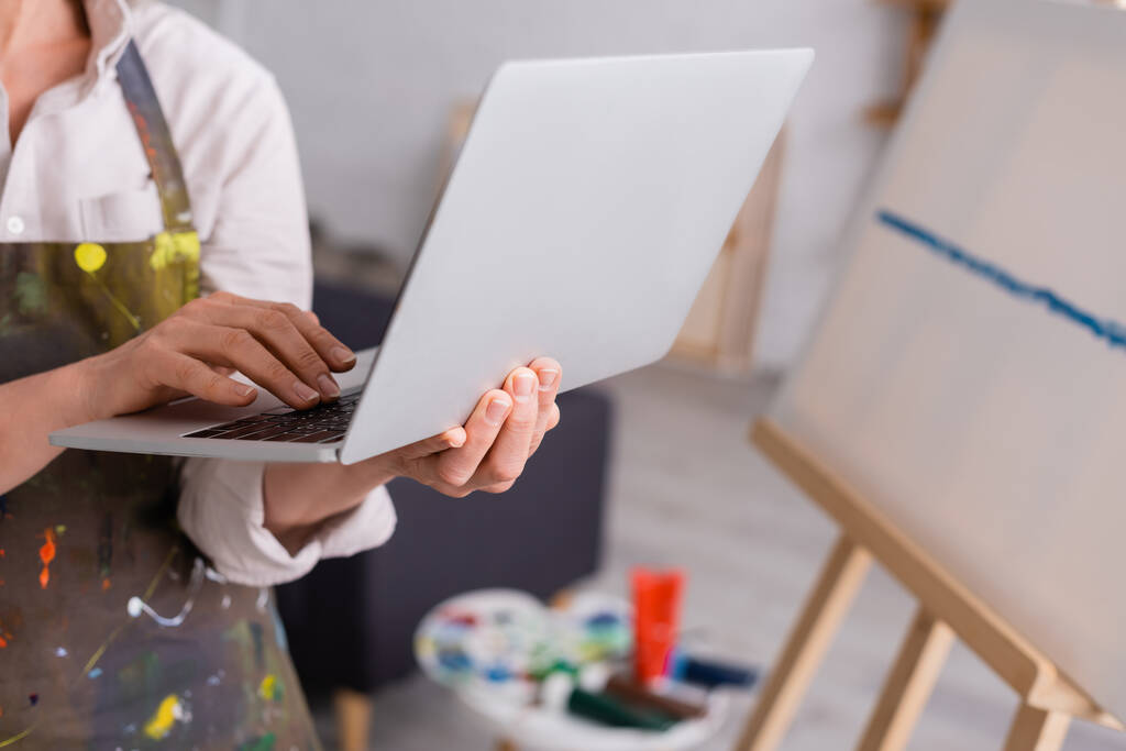частковий вид зрілої жінки, що тримає ноутбук під час перегляду підручника біля полотна
 - Фото, зображення