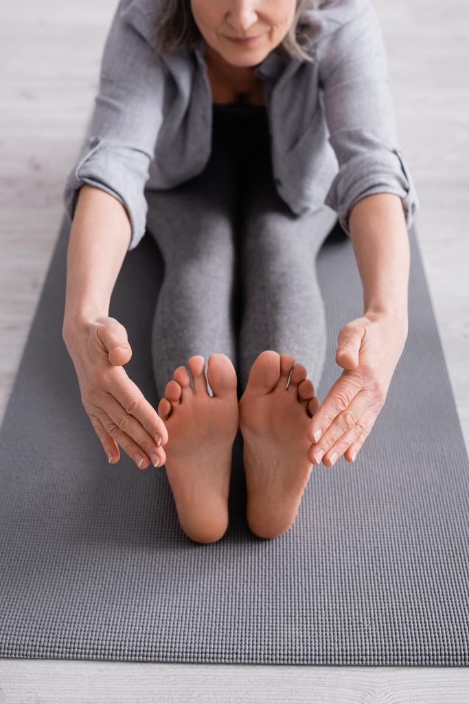 vista ritagliata di donna matura con capelli grigi che si estende su tappetino yoga  - Foto, immagini