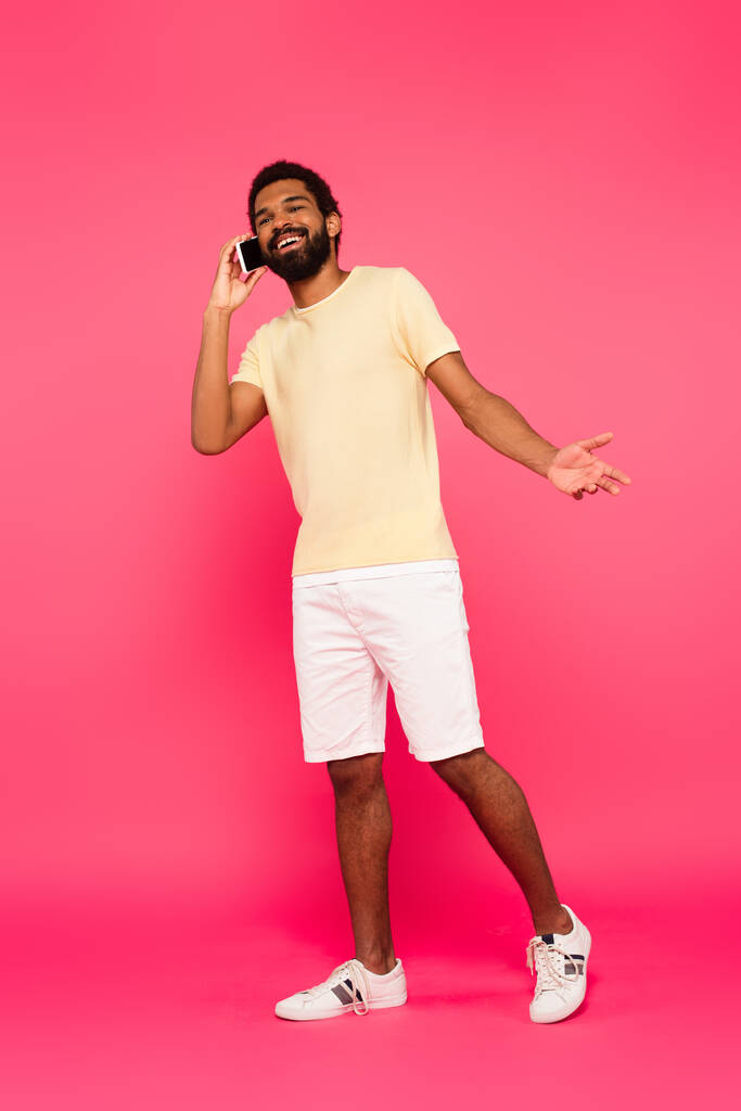 piena lunghezza di felice uomo africano americano parlando su smartphone su rosa - Foto, immagini