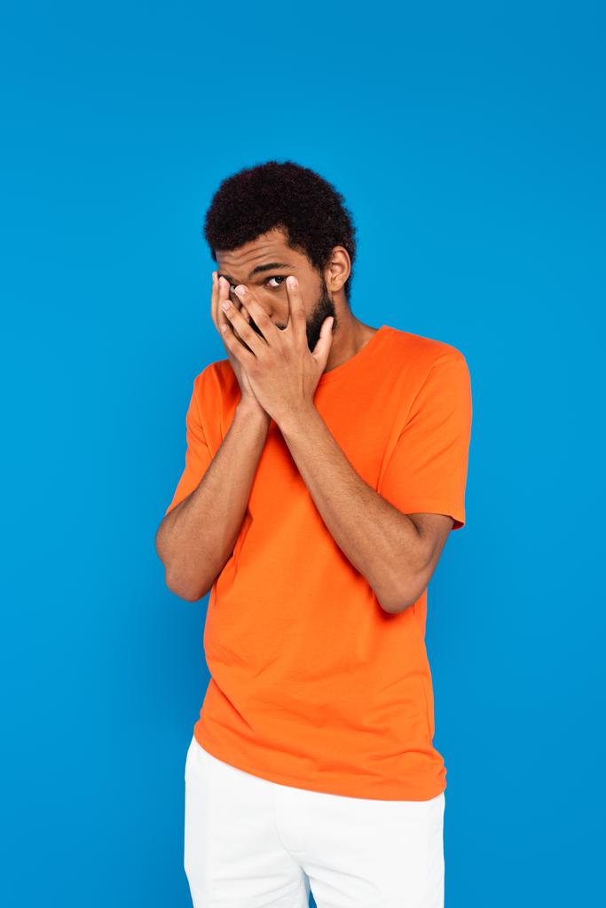 scared african american man covering face with hands isolated on blue - Photo, Image