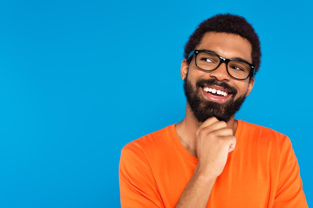χαμογελαστός Αφροαμερικάνος με γυαλιά κοιτάζει μακριά απομονωμένος στο μπλε - Φωτογραφία, εικόνα