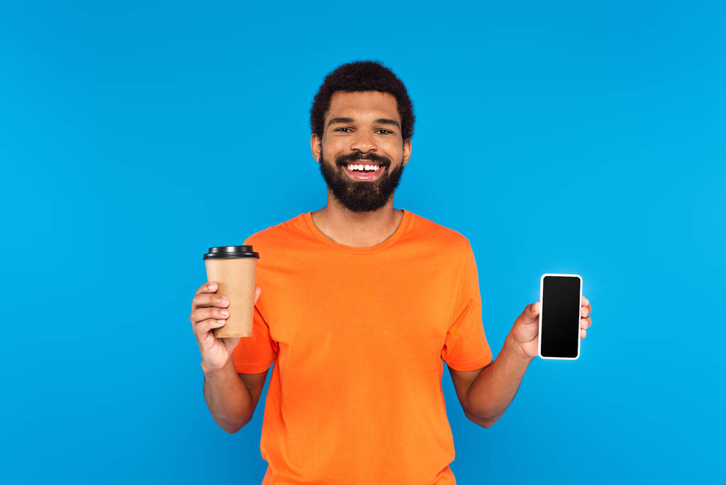 cheerful african american man holding paper cup and smartphone isolated on blue - Photo, Image