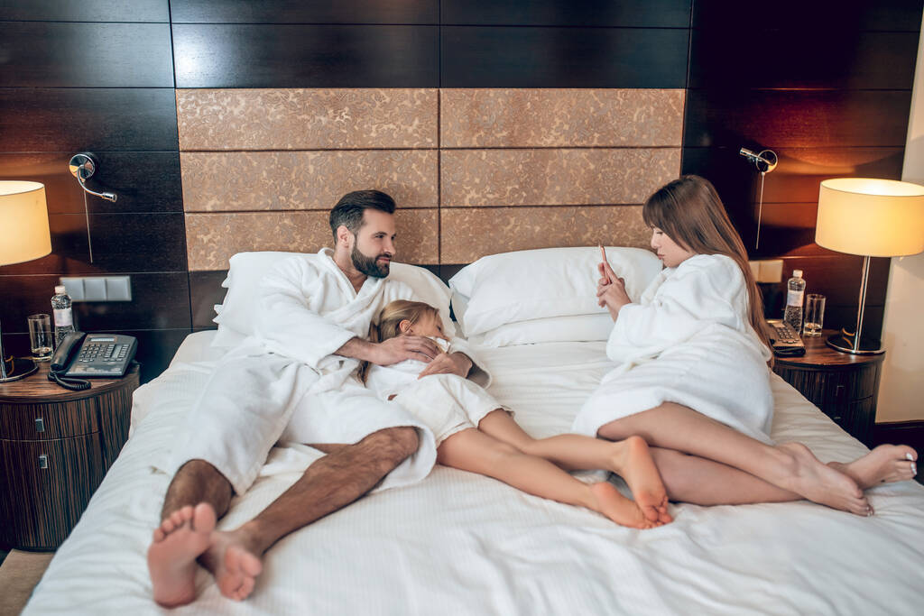 Сім'я в білому одязі лежить в ліжку і виглядає спокійно
 - Фото, зображення